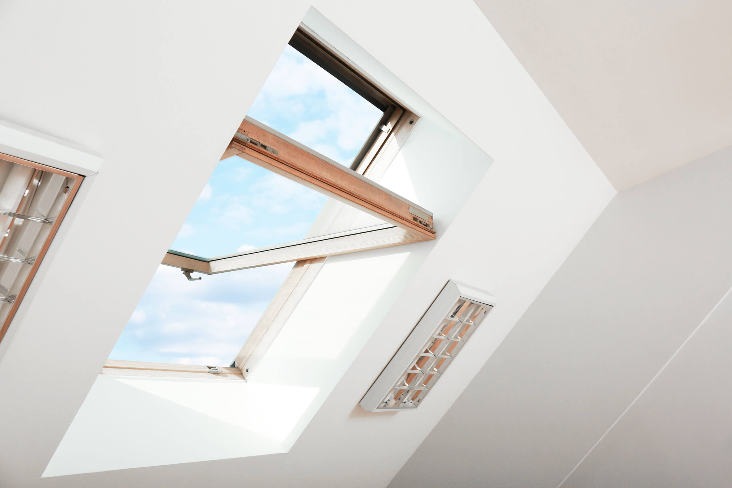 Open skylight window in sloped ceiling showing blue sky, used for heat ventilation.